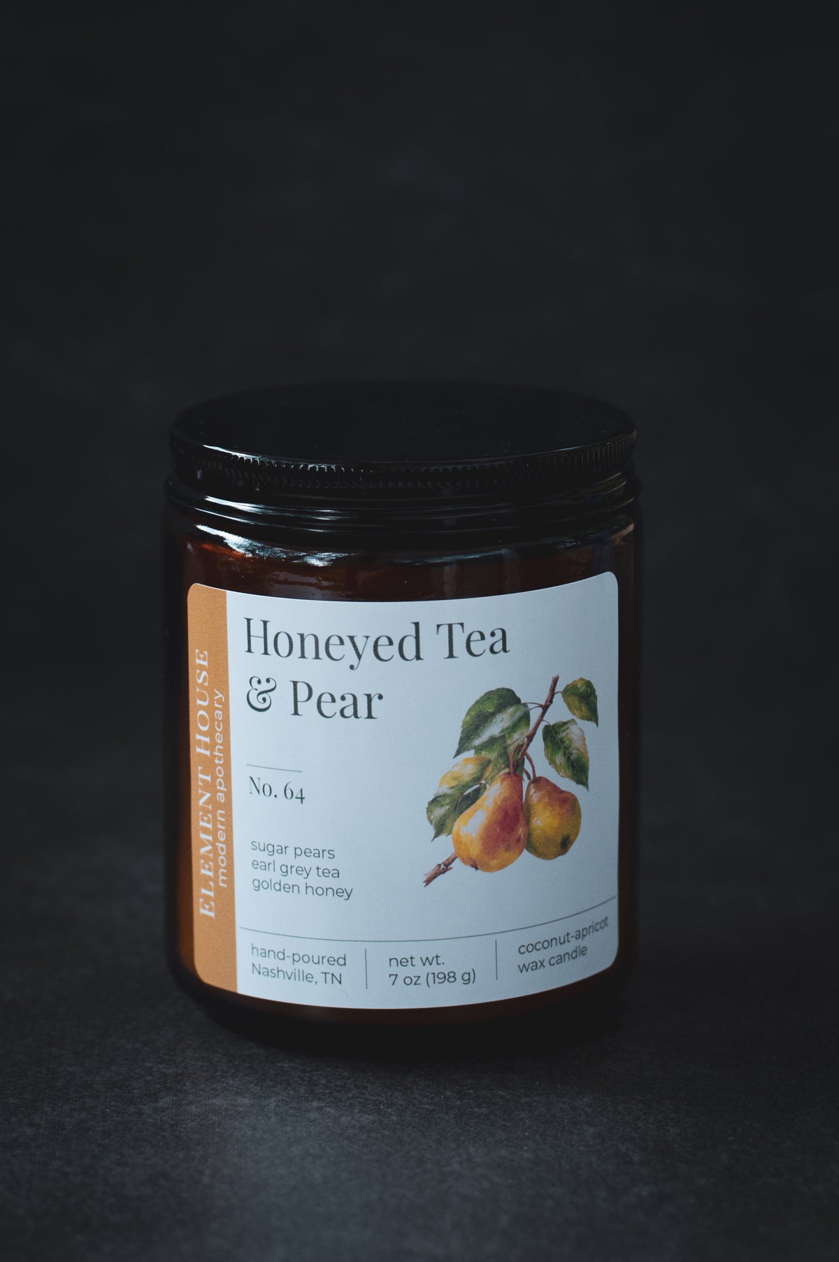 Honeyed Tea & Pear candle in an amber glass jar with a black lid, featuring a white Element House label with illustrated pears and No. 64, photographed against a dark background.