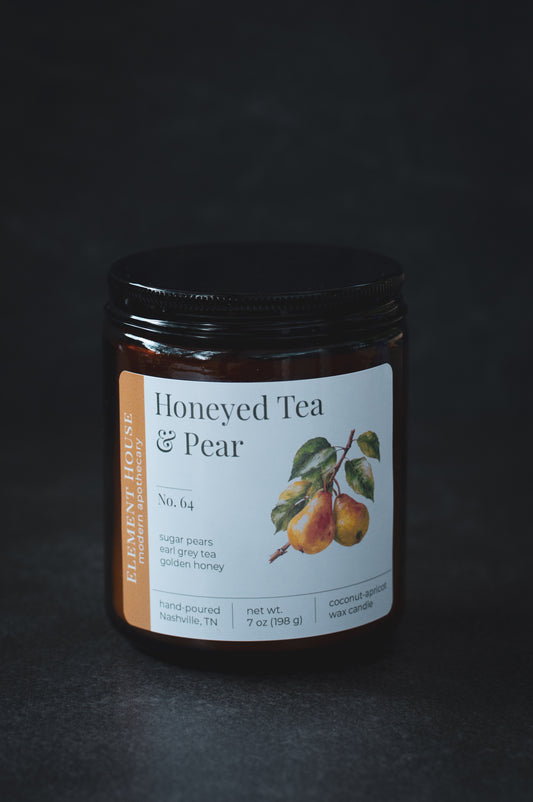 Honeyed Tea & Pear candle in an amber glass jar with a black lid, featuring a white Element House label with illustrated pears and No. 64, photographed against a dark background.