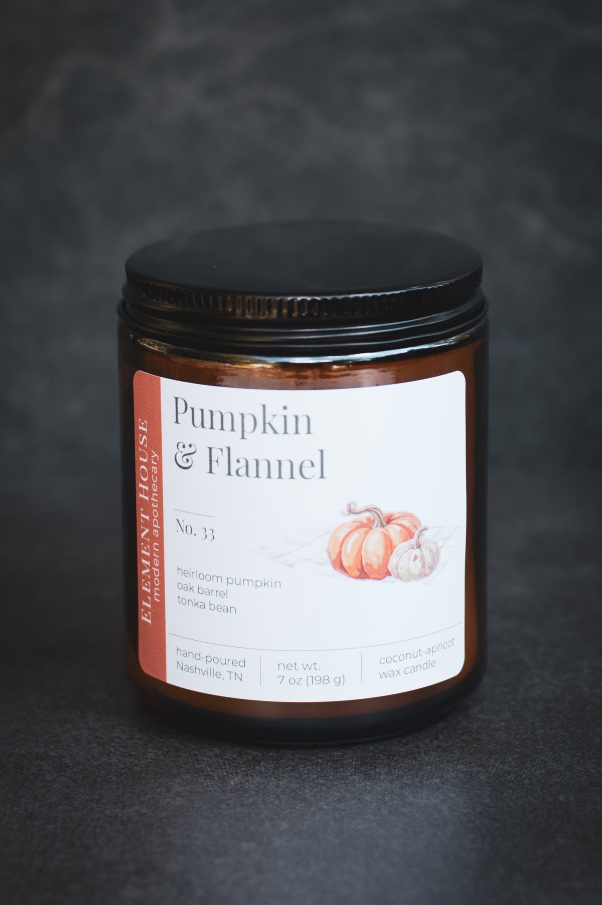 Pumpkin & Flannel candle in an amber glass jar with a black lid, featuring an Element House label with pumpkin illustrations, photographed against a dark textured background.