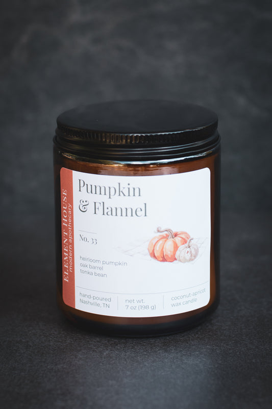 Pumpkin & Flannel candle in an amber glass jar with a black lid, featuring an Element House label with pumpkin illustrations, photographed against a dark textured background.