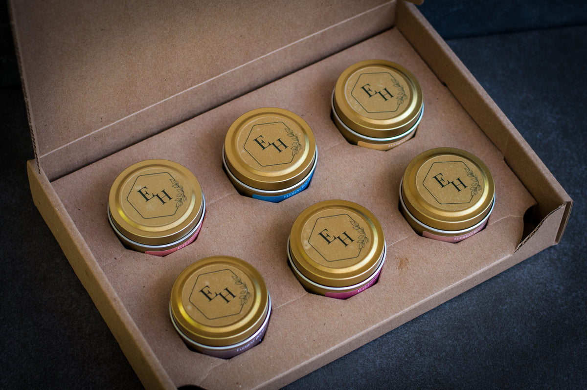 Element House Fall/Winter Discovery Box open to reveal six gold mini candle tins with EH monogram labels, arranged in a kraft gift box.