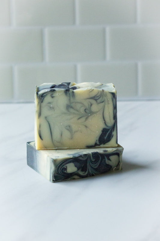 Handcrafted soap bar made with local Tennessee beer and scented with tobacco and bay leaf, featuring a natural cream and charcoal swirl design, displayed on a marble surface by Hen House Bath Co.